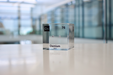 Piece of Osmium encased in a clear acrylic cube, with the element's name, atomic number, and properties displayed as on the periodic table for a sleek, educational display.