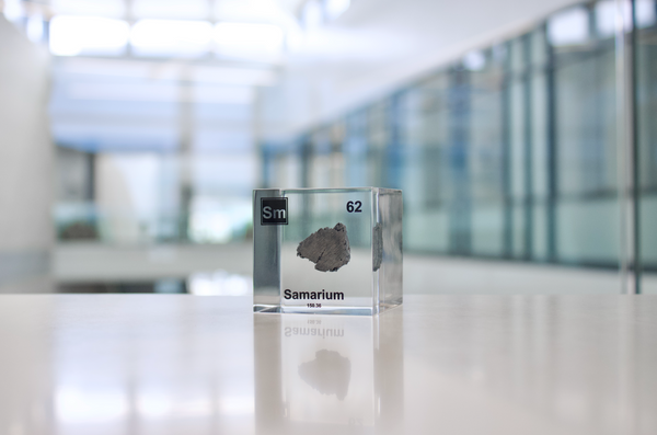 Clear acrylic cube displaying a Samarium element (Atomic Number 62) embedded within, offering a scientific presentation for collectors and science enthusiasts.