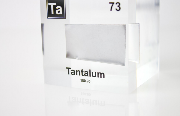 Clear acrylic cube displaying a Tantalum element (Atomic Number 73) embedded within, offering a scientific presentation for collectors and science enthusiasts.