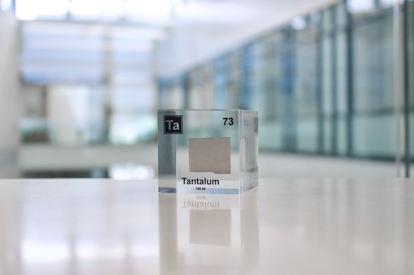 Clear acrylic cube displaying a Tantalum element (Atomic Number 73) embedded within, offering a scientific presentation for collectors and science enthusiasts.