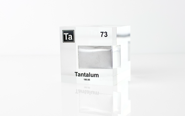 Clear acrylic cube displaying a Tantalum element (Atomic Number 73) embedded within, offering a scientific presentation for collectors and science enthusiasts.