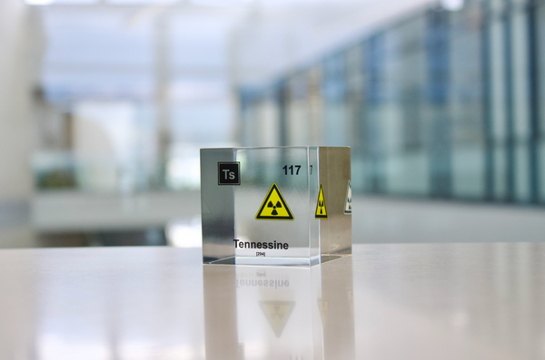 Clear acrylic cube displaying a Tennessine element (Atomic Number 117) embedded within, offering a scientific presentation for collectors and science enthusiasts.