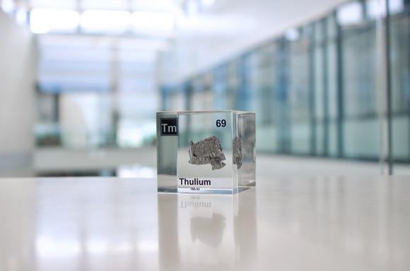 Clear acrylic cube displaying a Thulium element (Atomic Number 69) embedded within, offering a scientific presentation for collectors and science enthusiasts.