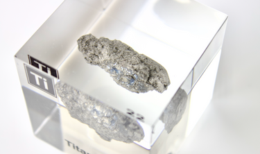 Clear acrylic cube displaying a Titanium element (Atomic Number 22) embedded within, offering a scientific presentation for collectors and science enthusiasts.
